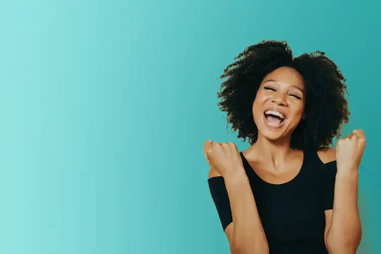 Smiling woman celebrating success with raised fists on teal background