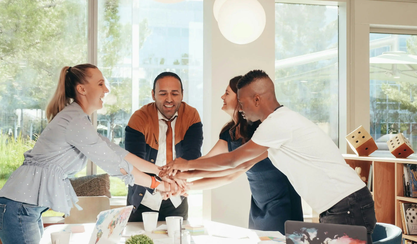 Diverse group of adults smiling and stacking hands in a bright office teamwork meeting